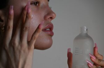 A close-up of a person's hands applying skincare products on their face, showcasing a variety of skincare items like serums and moisturizers.