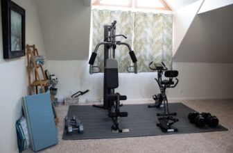 A cozy home gym with basic fitness equipment like dumbbells, a yoga mat, and resistance bands in a well-lit room.